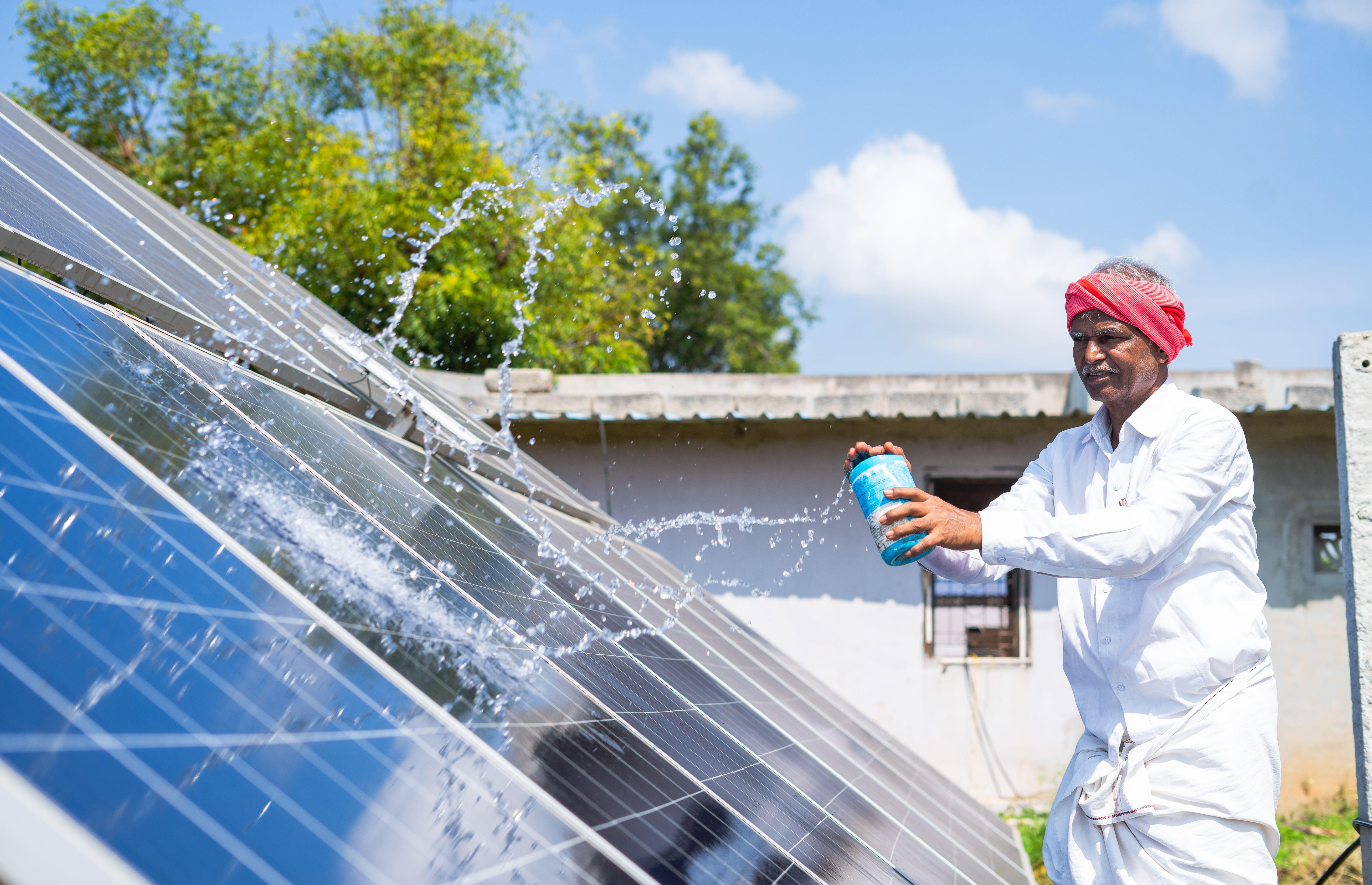 An Indian farmer cleans solar panels with water